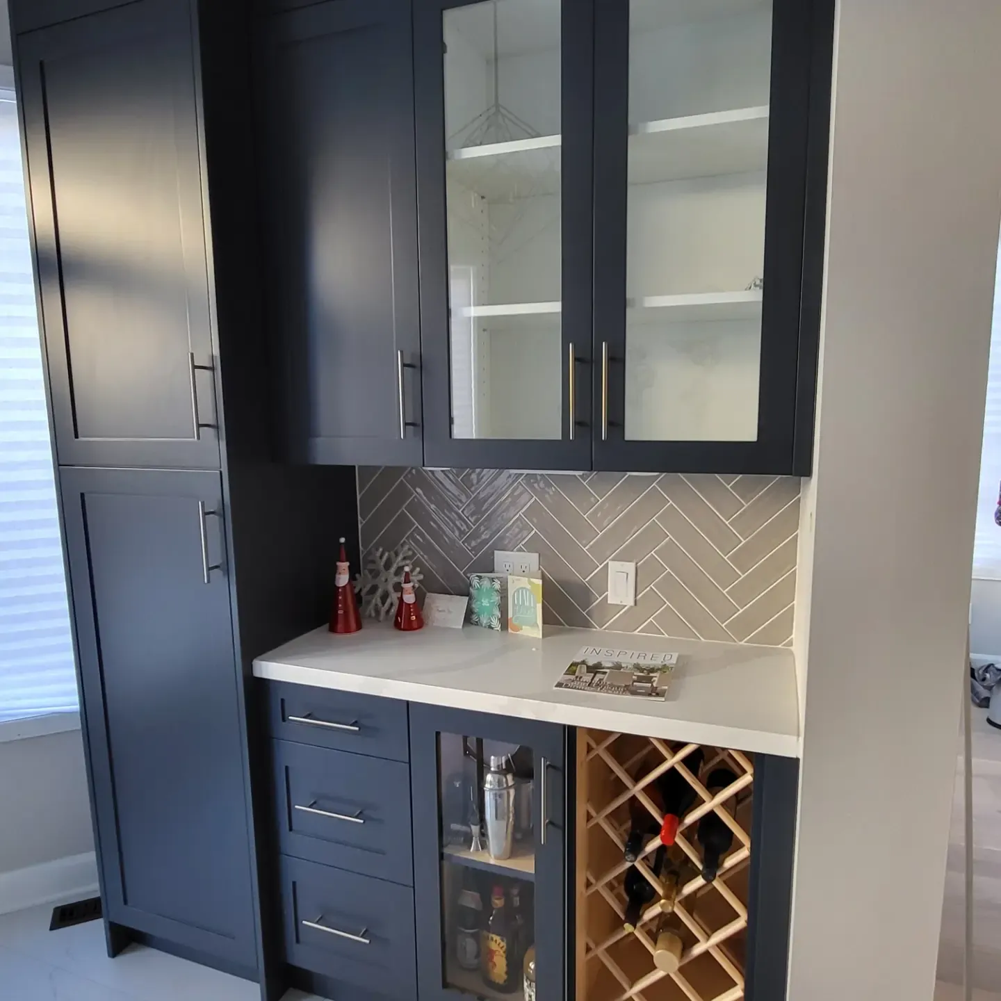 Dark navy built-in bar cabinets with wine rack, glass doors, white countertop, and herringbone tile backsplash