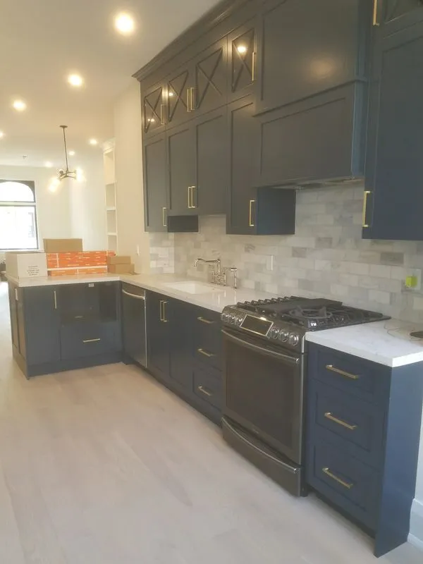 Navy blue kitchen cabinets with brass hardware, marble countertop, subway tile backsplash, and gas range mid-installation
