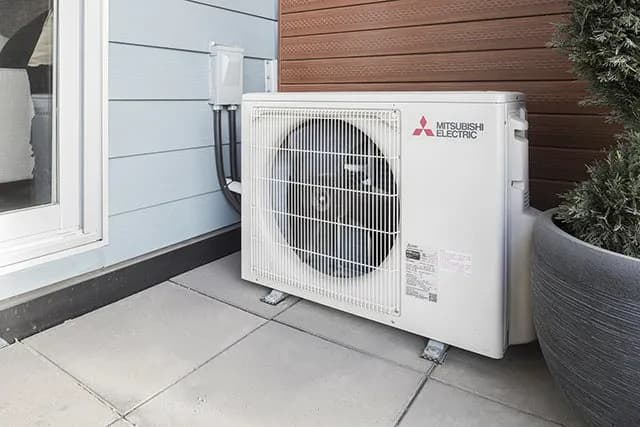 Mitsubishi Electric outdoor heat pump unit on concrete patio beside modern home