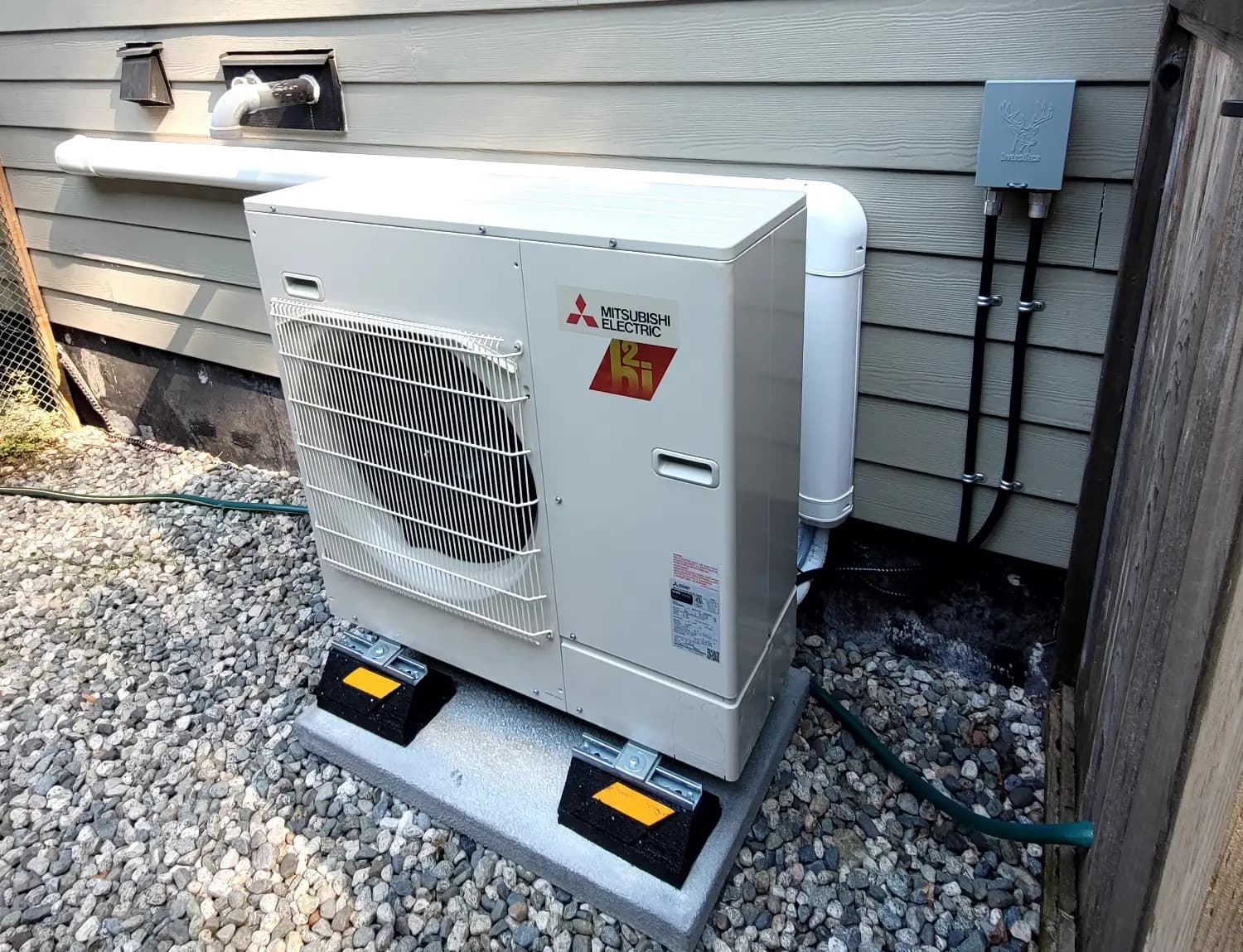 Mitsubishi mini-split condenser on concrete pad with refrigerant lines and electrical