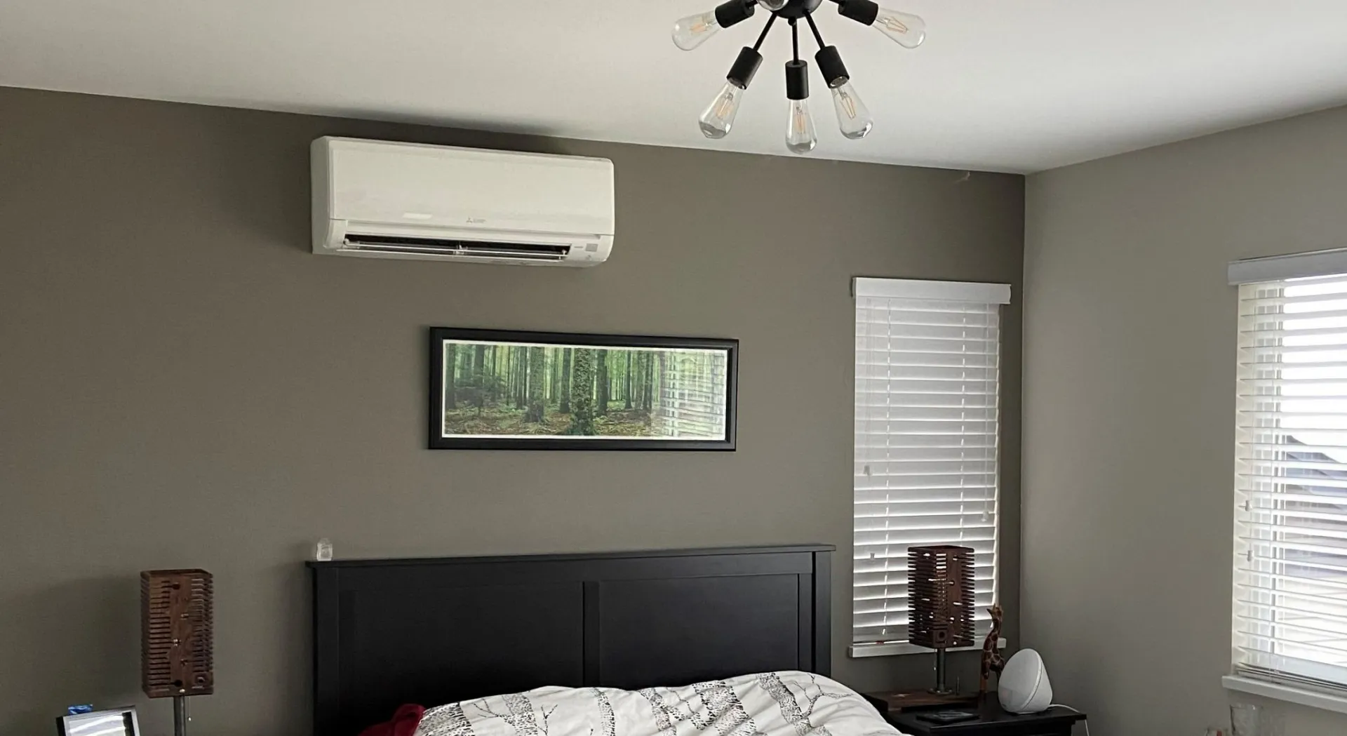 White mini-split air handler mounted on gray bedroom wall above dark headboard