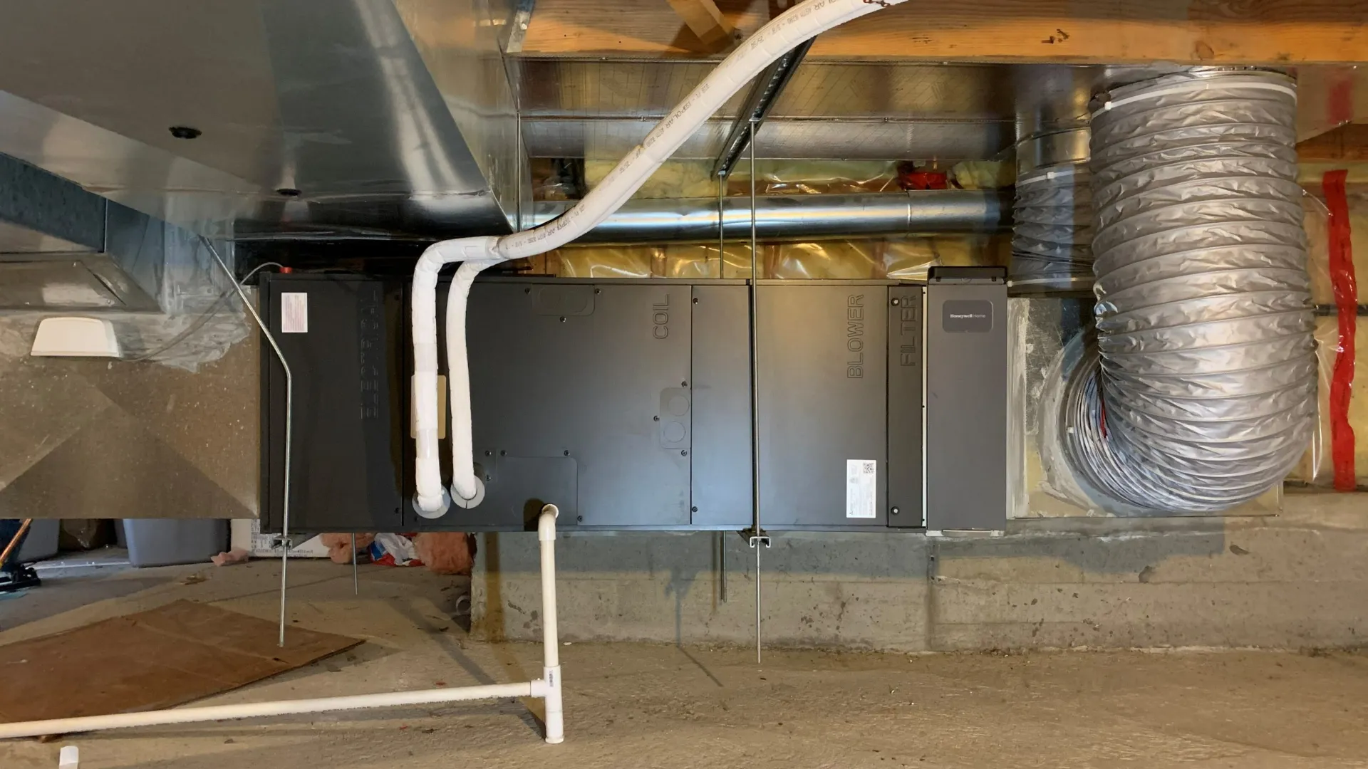 HVAC air handler unit mounted in basement with white PVC piping and flexible ductwork