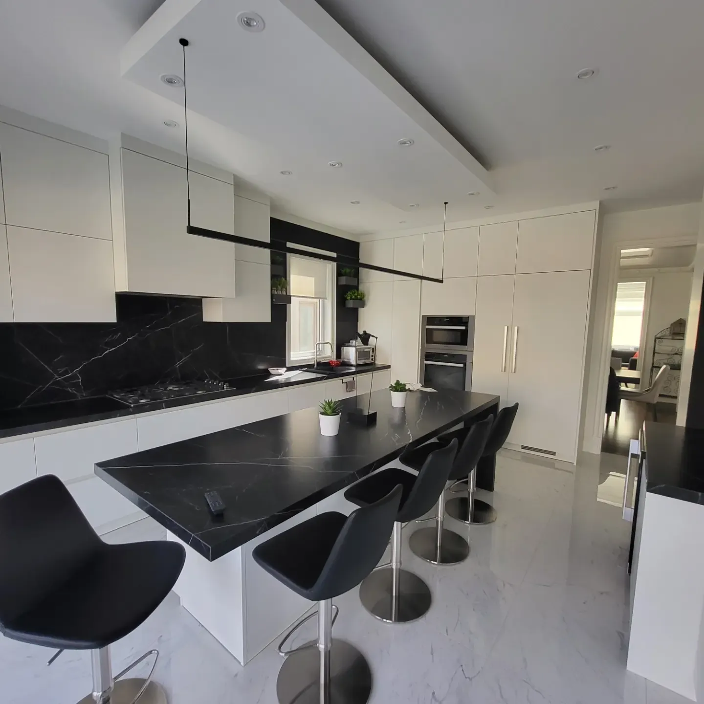 Modern black and white kitchen with marble island, bar stools, and recessed ceiling lighting in Oakville home