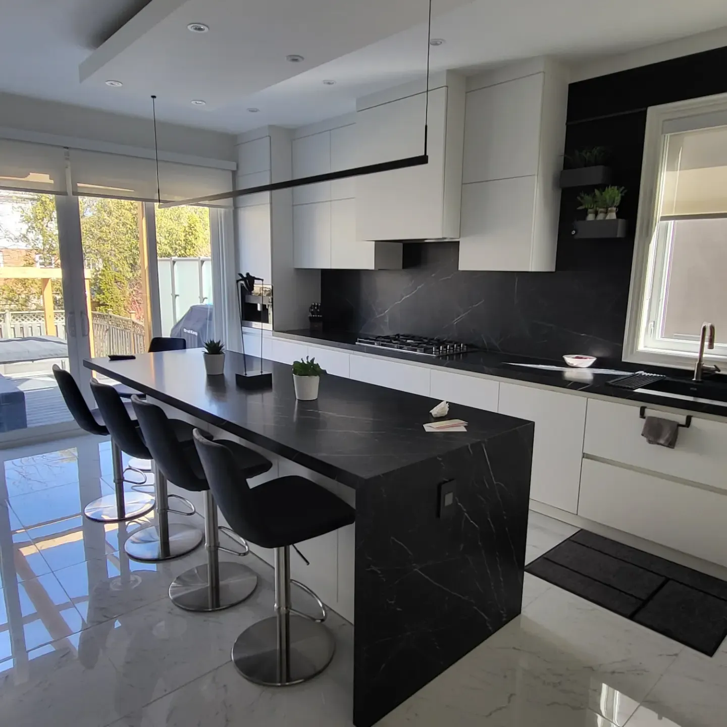 Bright modern kitchen with black marble island, white cabinetry, and large sliding glass doors in Oakville